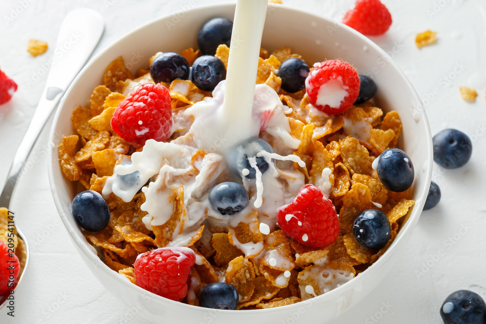 Healthy Morning Breakfast honey Corn flakes with fresh fruits of Raspberry, blueberries and pouring milk in bowl.