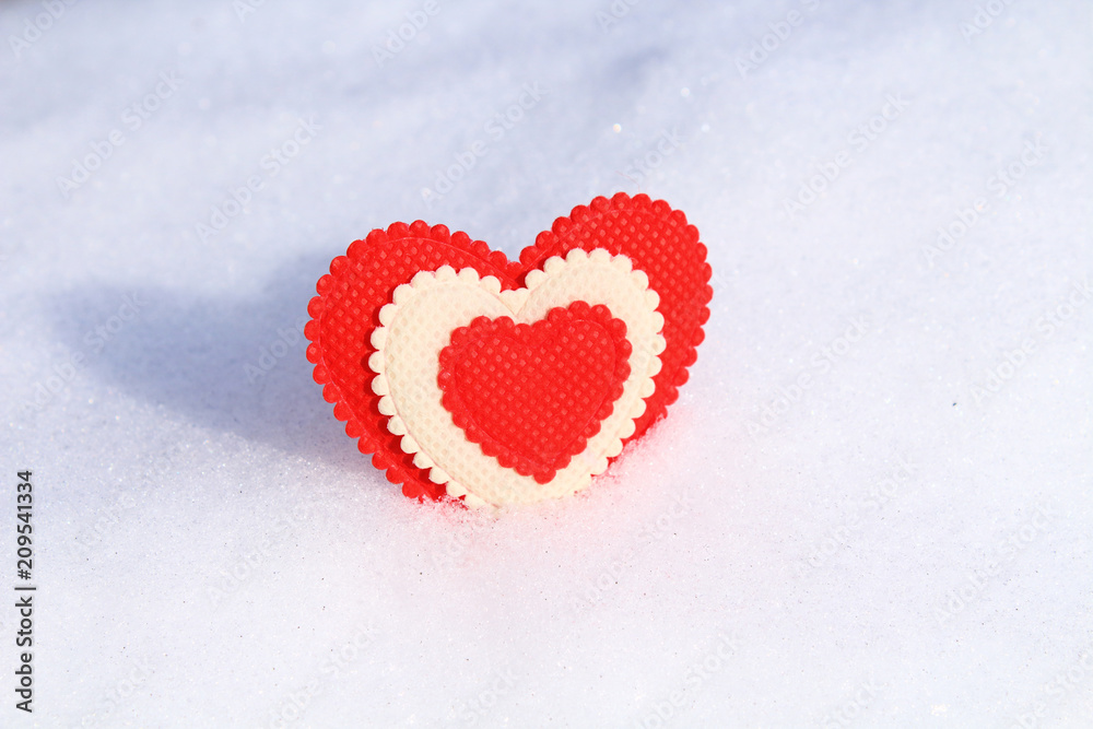A beautiful red soft heart made of cloth in cold snow. Background. Close-up.