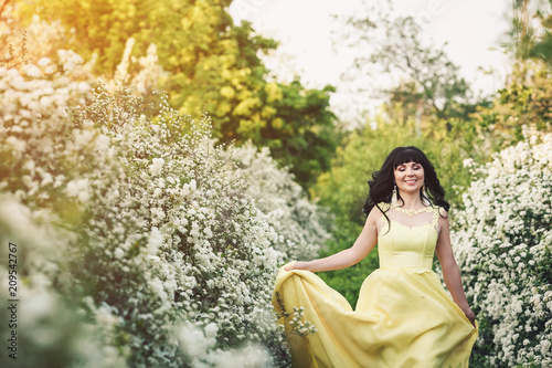 girl in yellow dress is standing between flowering spiraea and sunbeam shines on her.