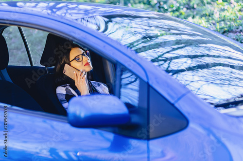 Girl is sitting at wheel of car and talking by phone
