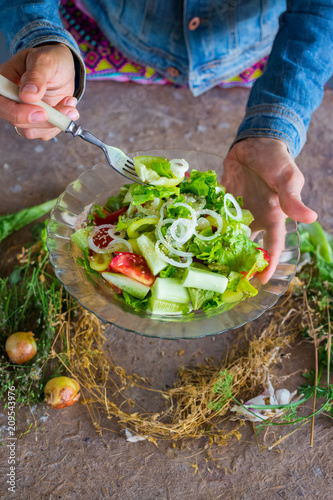 Woman hands holds, tastes vegetables salad with fork. Cucumbers, tomatoes, onion rings, unrefined sunflower oil, rock salt. Raw vegan vegetarian healthy food