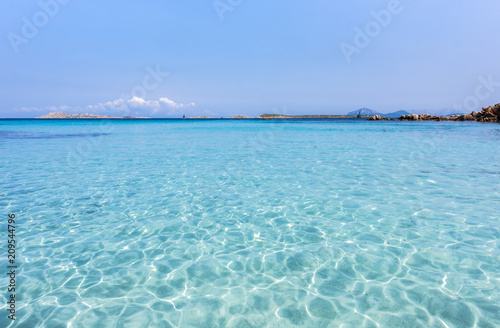 Inviting turquoise mediterranean sea with reflections - mountain range and rocks in the background, Capriccioli beach, Sardinia, Italy