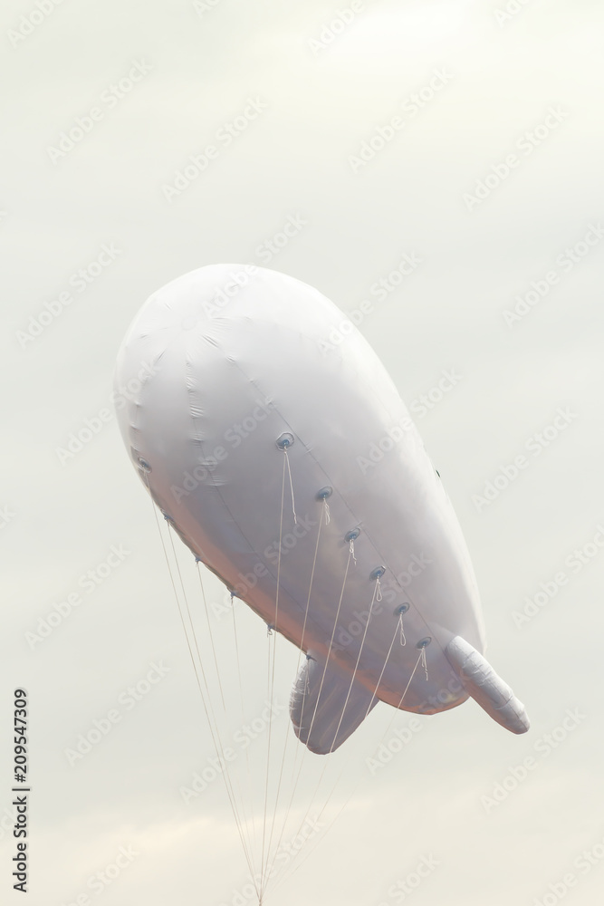 Fototapeta premium White inflatable dirigible with a place for a logo on a background of a gray sky with clouds