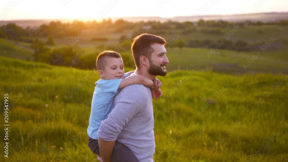 Son embracing father while sitting on his back walking in field Son embracing father while sitting on his back walking in field