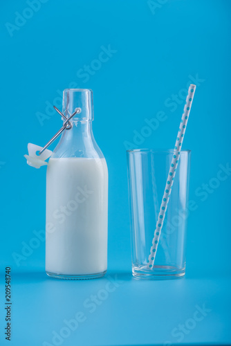 Glass bottle of fresh milk and a glass with a straw on a blue background. Concept of healthy dairy products with calcium