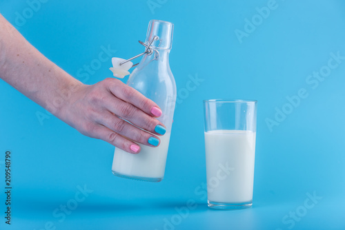 Woman's hand pours fresh milk from a bottle into a glass on a blue background. Concept of healthy dairy products