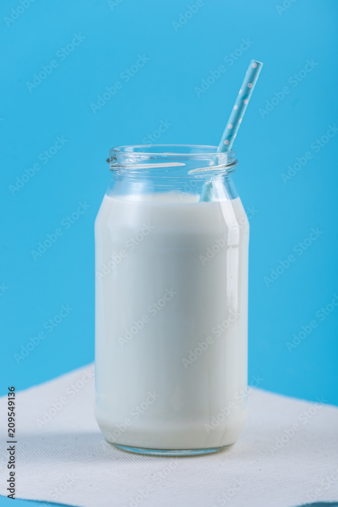Glass bottle of fresh milk with straw on blue background. Colorful minimalism. Healthy dairy products with calcium