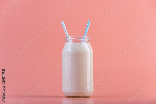 Glass bottle of fresh milk with two straws on pink background. Colorful minimalism. Healthy dairy products with calcium