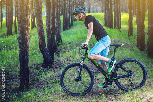 Man in a helmet riding on a green mountain bike in the woods. Cyclist in motion. Concept of active and healthy lifestyle