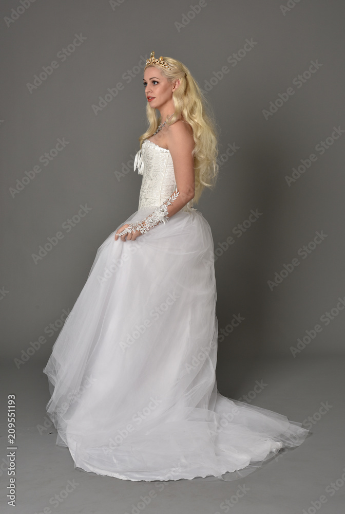 full length portrait of blonde girl wearing white fantasy gown. standing pose in side profile, grey studio background. full length portrait of blonde girl wearing white fantasy gown. standing pose in side profile, grey studio background.