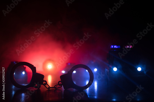 Fotografia, Obraz Closed handcuffs on the street pavement at night with police car lights