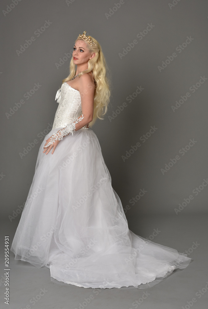 full length portrait of blonde girl wearing white fantasy gown. standing pose in side profile, grey studio background. full length portrait of blonde girl wearing white fantasy gown. standing pose in side profile, grey studio background.