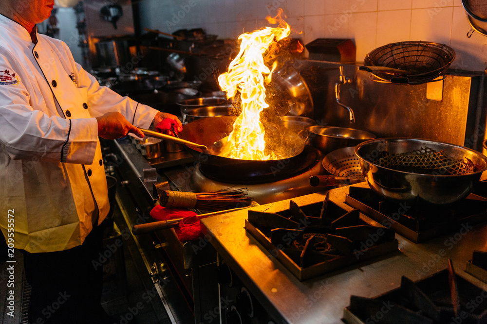 Chef cooking Chinese food with burning fire on steel pan.