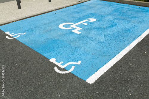 International handicapped symbol painted in bright blue on a shopping center parking space. The space is clearly marked on either side with additional white diagonal stripes.