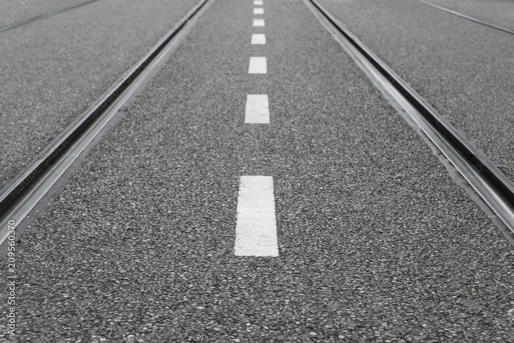 Empty city street with white dotted line and parallel tram tracks Empty city street with white dotted line and parallel tram tracks