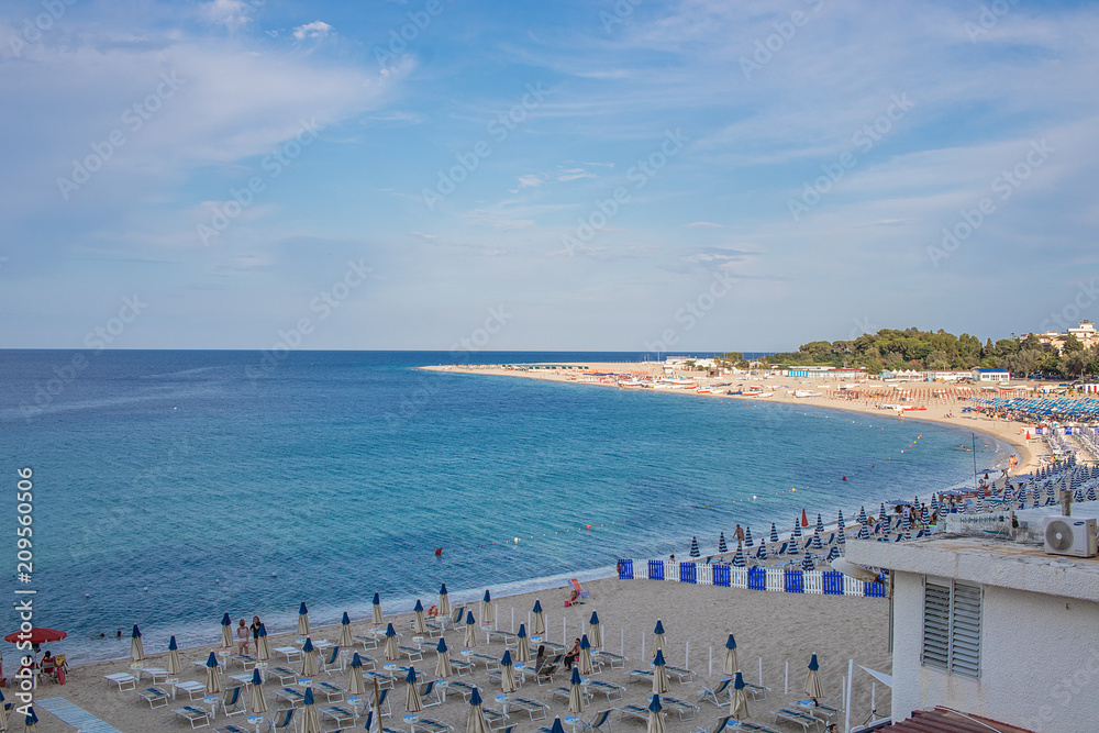 Paesaggio Mare Sud Italia, Europa. Calabria, Soverato. Mare urchese, cielo blu con nuvole. Ombrelloni e sedie da mare in spiaggia