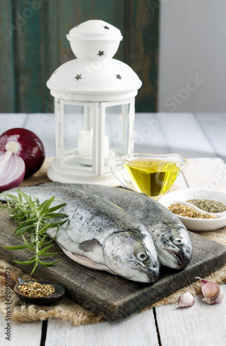 Two rainbow trouts on rustic wooden table among herbs and vegetables photo