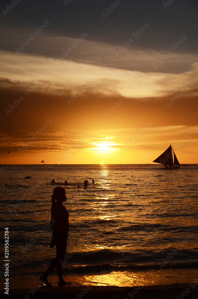 Sunset time at a beautiful island with orange gradient colour of sky and people playing around the beach.
