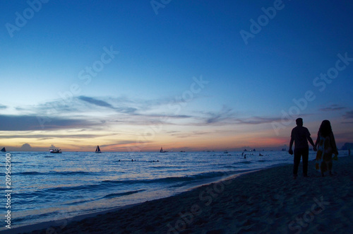 Sunset time at a beautiful island with orange gradient colour of sky and people playing around the beach.