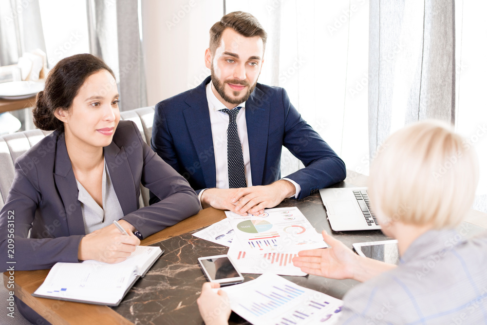 Content confident team of financial experts in formalwear sitting at table and talking to customer at meeting, unrecognizable woman asking questions about data Content confident team of financial experts in formalwear sitting at table and talking to customer at meeting, unrecognizable woman asking questions about data
