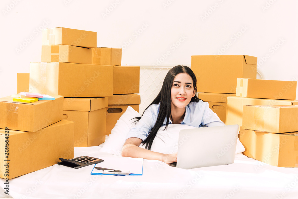 Young woman freelancer working and use laptop computer with cardboard box on bed at home - SME business online and delivery concept Young woman freelancer working and use laptop computer with cardboard box on bed at home - SME business online and delivery concept
