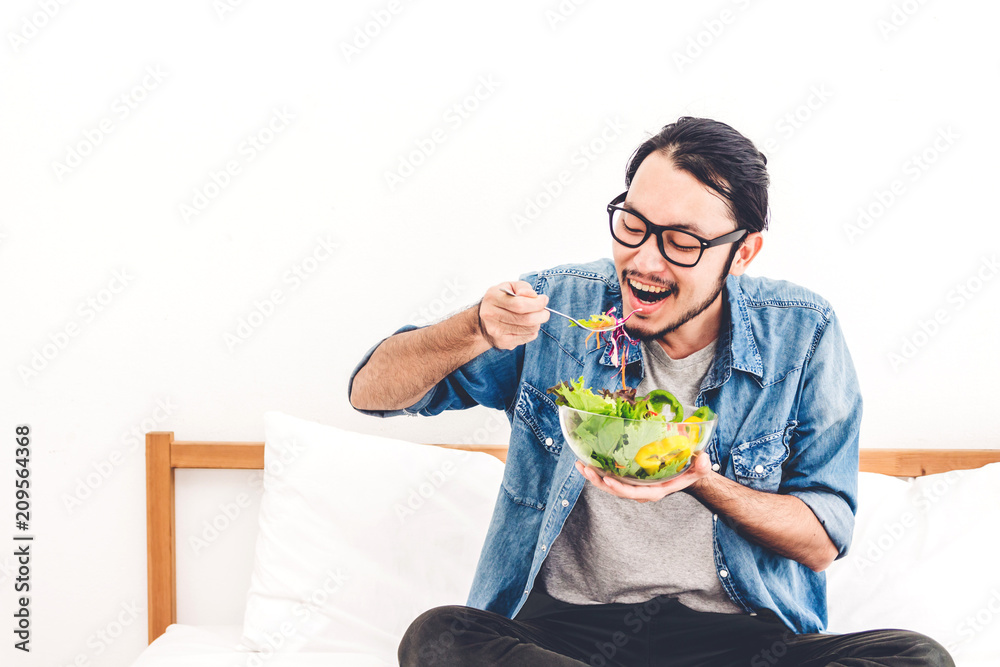 Young man eating organic healthy salad with vegetable in bowl on bed at home.diet food and healthy life concept Young man eating organic healthy salad with vegetable in bowl on bed at home.diet food and healthy life concept