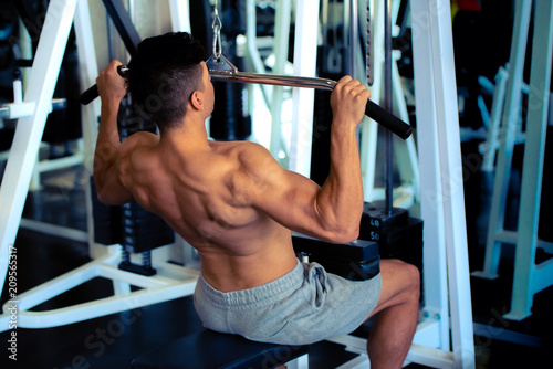 Portrait of young man doing exercise by using weight lifting equipment in sport gym, bodybuilder concept.
