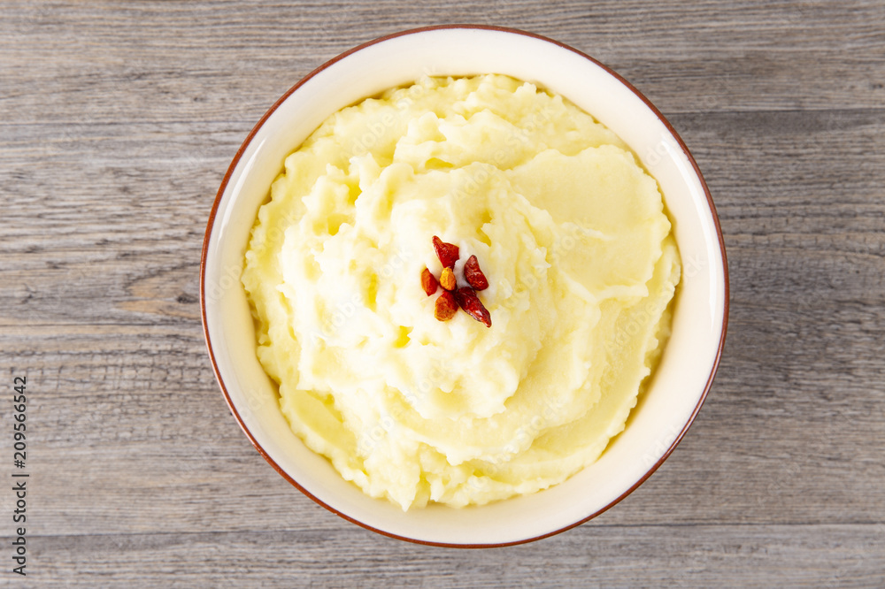 Puree from potatoes in a plate. Red pepper in the middle. Wooden background. Macro. Puree from potatoes in a plate. Red pepper in the middle. Wooden background. Macro.