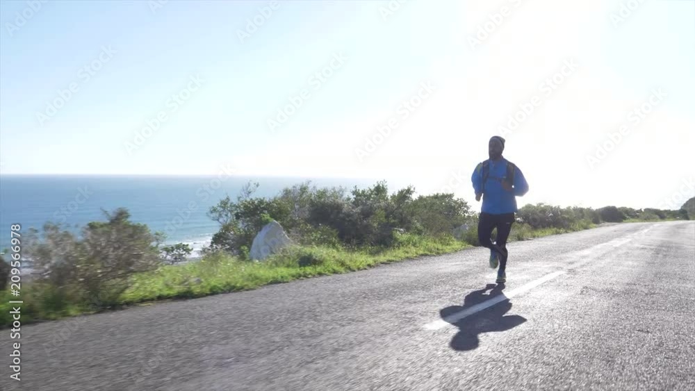Tracking shot of Mixed race man running alone down a country road overlooking the sea Tracking shot of Mixed race man running alone down a country road overlooking the sea