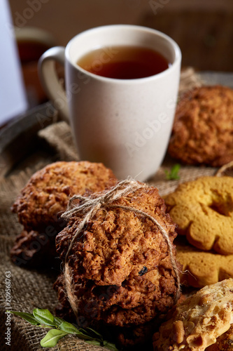 Conceptual festive composition with a cup of hot tea, cookies and spicies on a wooden barrel, selective focus, close-up