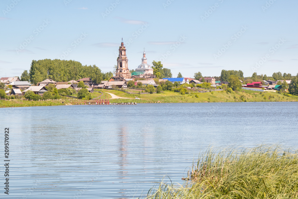 Russian village landscape. Lake with houses and old church in the background