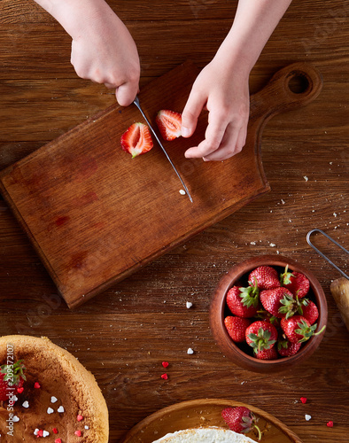 Top view of girl's hands putting strawberries on cake, close-up, selctive focus, vertical. photo