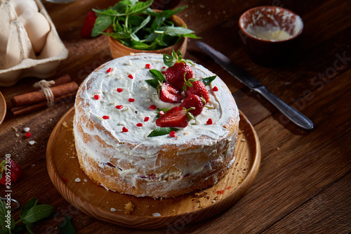 Strawberry tart covered with whipped sour cream on a wooden tray over rustic background, selective focus photo