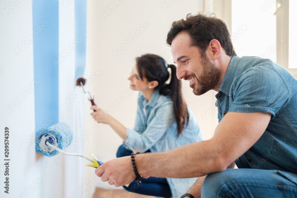 Renovation diy paint couple in new home painting wall together - obrazy, fototapety, plakaty 