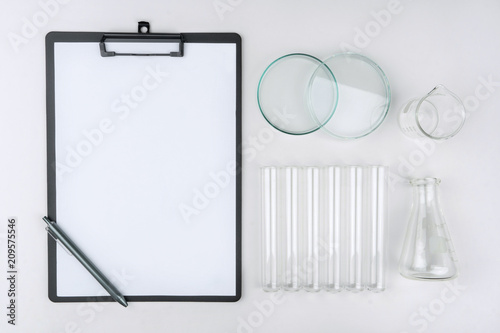 top view of laboratory equipments. A clipboard with pen, flask, test tubes, watch glass and beaker on the table