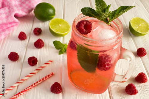 Cold lemonade with raspberries, lime and mint on the white wooden background