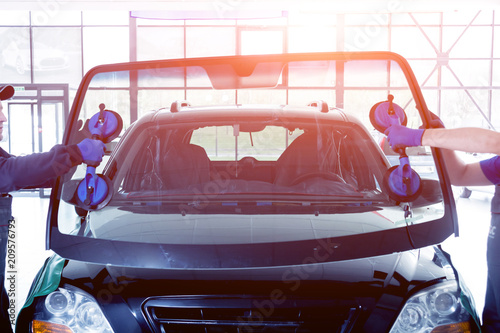 Automobile special workers replacing windscreen or windshield of a car in auto service station garage. photo