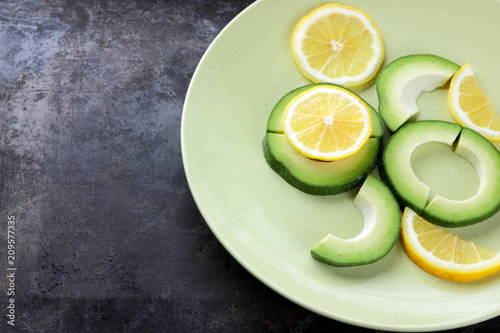 Sliced avocado and lemons on a green plate, avocado on a dark vintage background, vegetarian food, healthy natural food, tropical fruits for breakfast, copy space Sliced avocado and lemons on a green plate, avocado on a dark vintage background, vegetarian food, healthy natural food, tropical fruits for breakfast, copy space