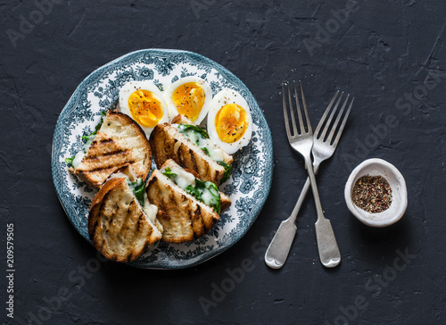 Healthy breakfast or snack - boiled farm eggs, spinach, grilled cheese sandwiches on dark background, top view