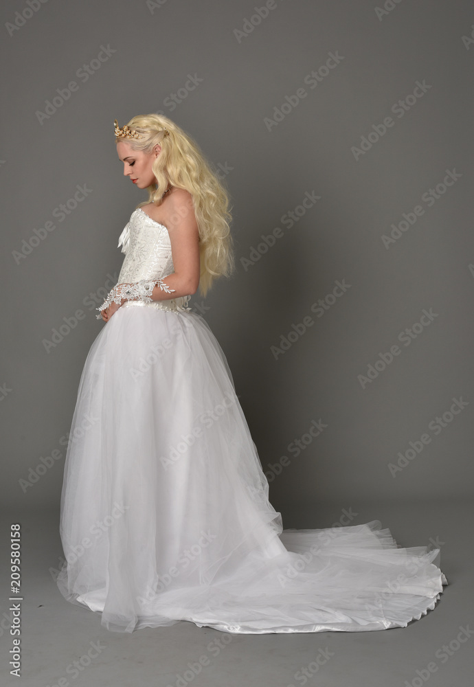 full length portrait of blonde girl wearing white fantasy gown. standing pose in side profile, grey studio background. full length portrait of blonde girl wearing white fantasy gown. standing pose in side profile, grey studio background.