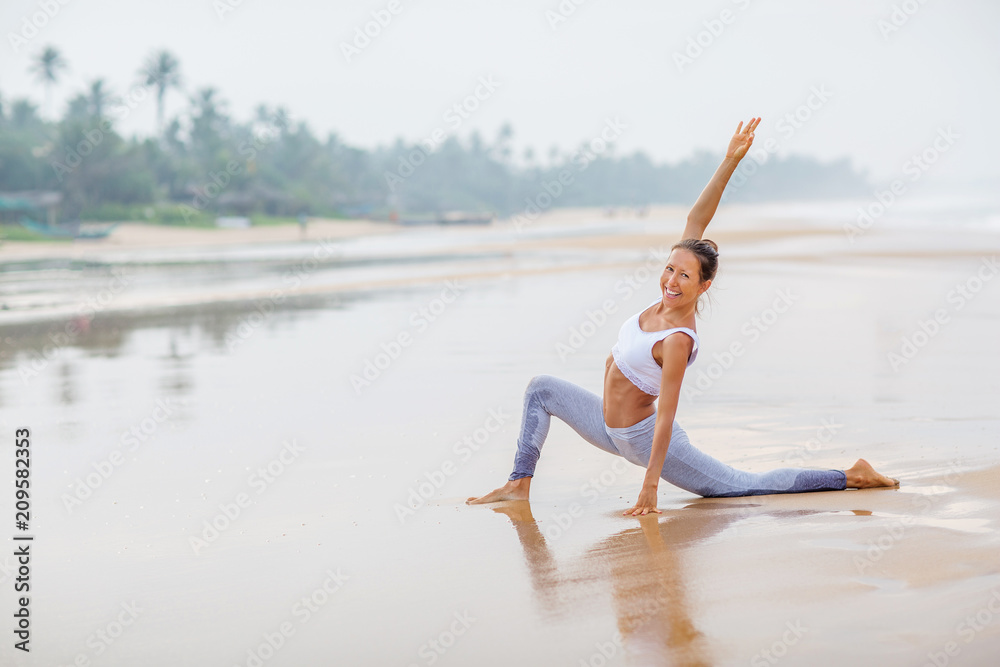 Fototapeta premium Caucasian woman practicing yoga at seashore of tropic ocean