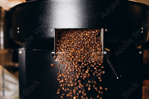 Fotografie Freshly roasted coffee beans pouring from a large coffee roaster into the cooling cylinder