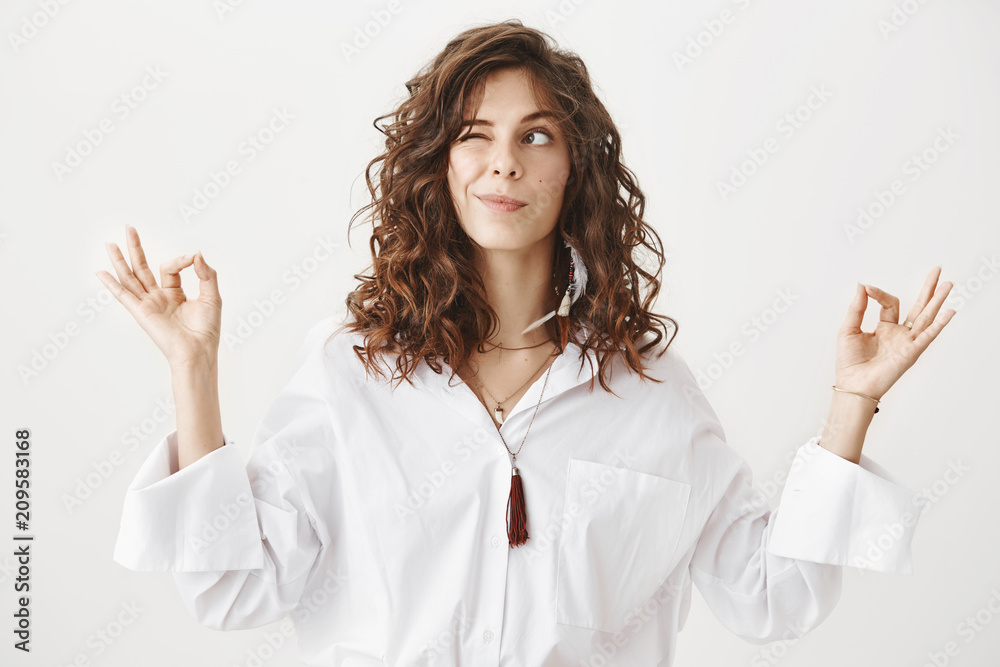 Studio portrait of charming positive caucasian female businesswoman trying to relax while meditating, standing with lifted hands and zen signs over gray background, peeking and looking aside playfully Studio portrait of charming positive caucasian female businesswoman trying to relax while meditating, standing with lifted hands and zen signs over gray background, peeking and looking aside playfully