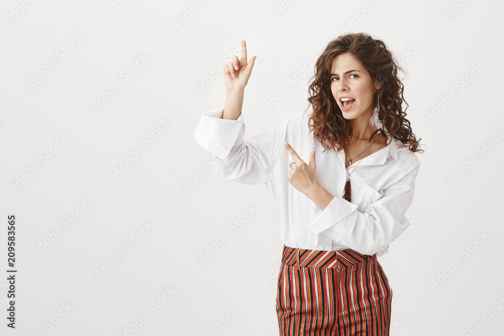Yeah look here. Portrait of confident good-looking european woman with curly hair, gazing self-assured at camera while pointing up with finger gun gesture, giving great advice or suggestion Yeah look here. Portrait of confident good-looking european woman with curly hair, gazing self-assured at camera while pointing up with finger gun gesture, giving great advice or suggestion