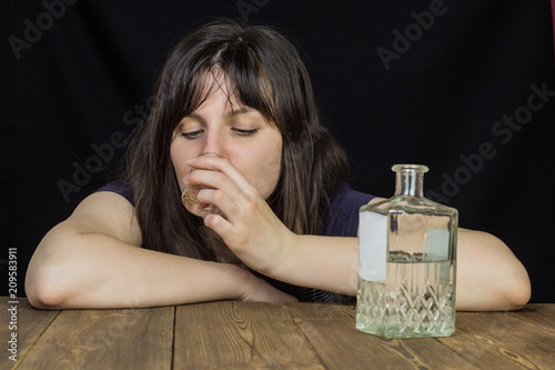 Konstfotografi A girl drinks alcohol from a wine-glass on the table is a bottle with alcohol, a