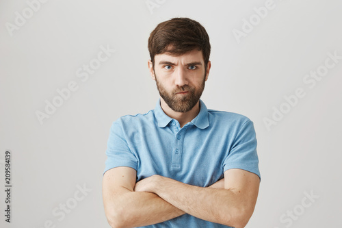 How should I punish you for such behavior. Portrait of bothered angry mature guy with beard standing with crossed hands and frowning, looking with mad expression at camera, being offended