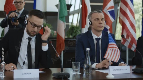 Representative men of different countries sitting at table on conference and listening to speech interpretation in headphones photo