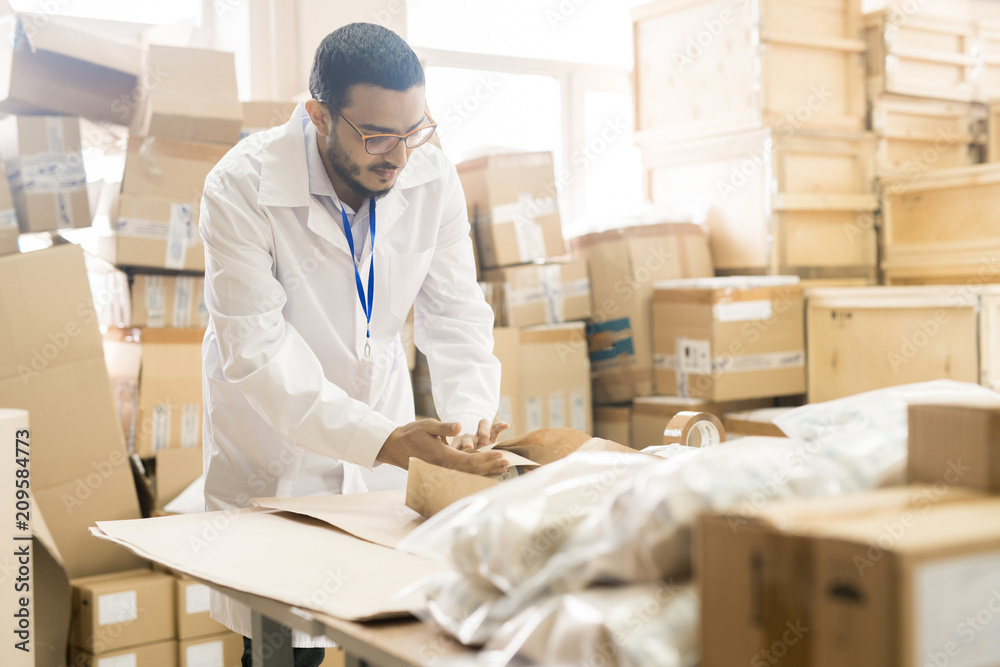Handsome Arabian worker wearing lab coat preparing production lot for delivery while working at warehouse of pressure sensor factory Handsome Arabian worker wearing lab coat preparing production lot for delivery while working at warehouse of pressure sensor factory