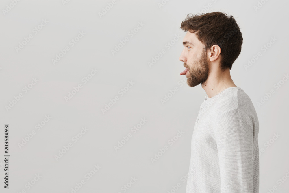 Profile portrait of childish happy adult man with beard sticking out tongue while standing over gray background. Playful mature man fools around while making breakfast with girlfriend Profile portrait of childish happy adult man with beard sticking out tongue while standing over gray background. Playful mature man fools around while making breakfast with girlfriend
