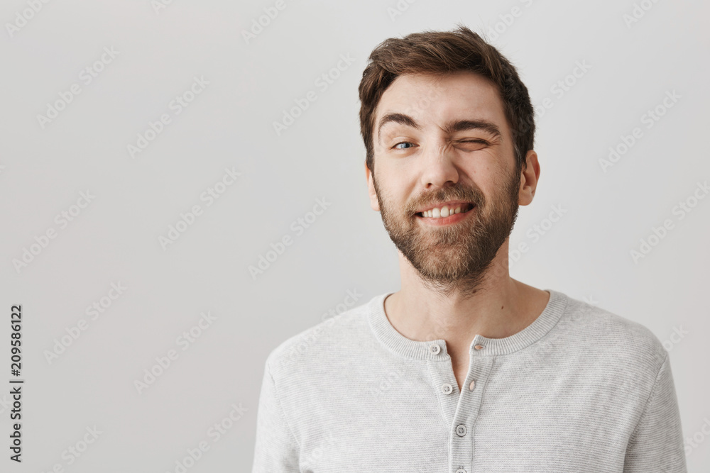 Emotions concept. Cute adult boyfriend winking and smiling, being in good, playful mood and standing over gray background. Guy gets to know his new peers. Man uses charm to impress girl he likes Emotions concept. Cute adult boyfriend winking and smiling, being in good, playful mood and standing over gray background. Guy gets to know his new peers. Man uses charm to impress girl he likes